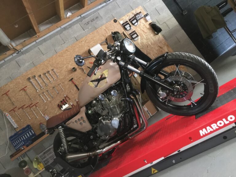 Café racer sur le pont élévateur rouge de l'atelier, devant le panneau de clés et d'outils accroché au mur