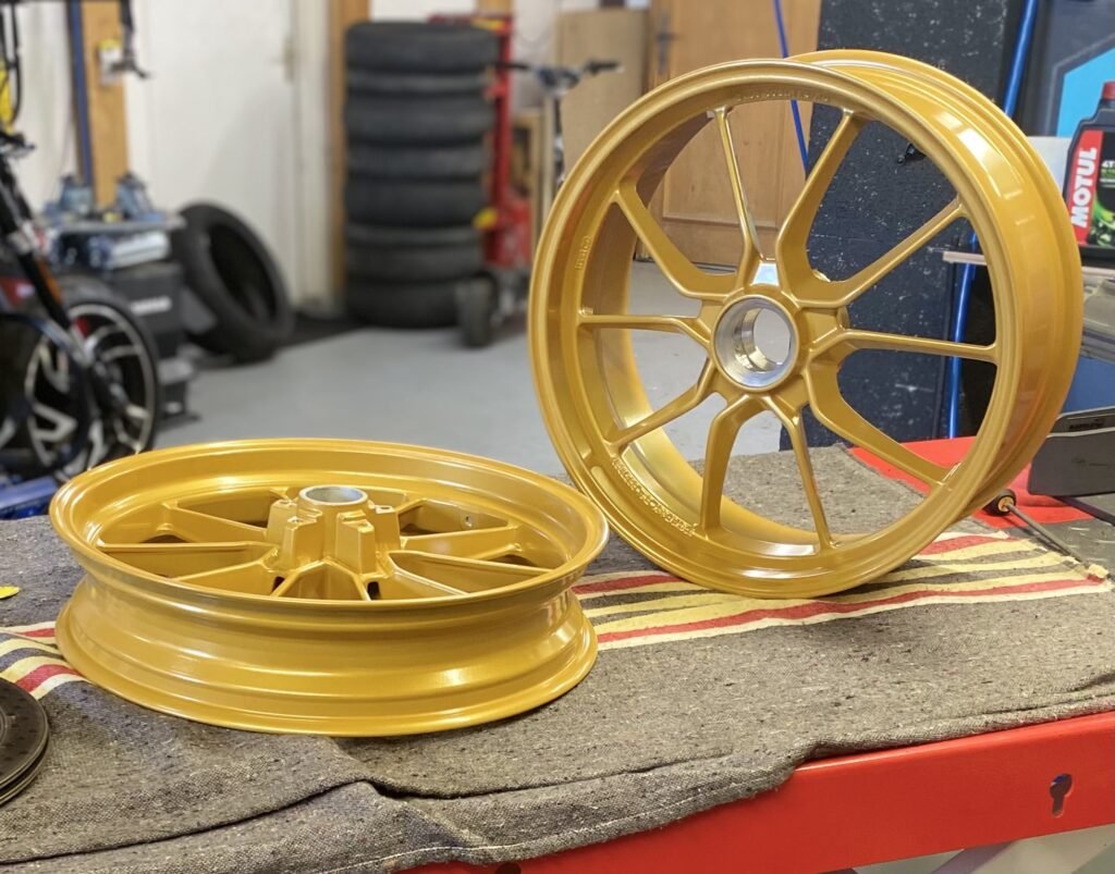 Paire de jantes Ducati Streetfighter repeintes en or sur l'établi, pile de pneus en arrière-plan