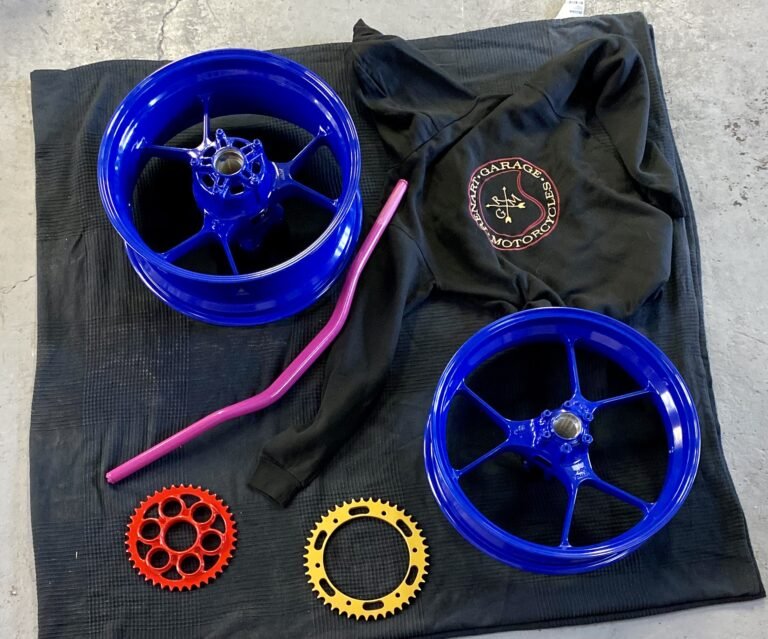 Deux jantes de moto repeintes en bleu, couronnes et guidon posés sur un drap à l'atelier